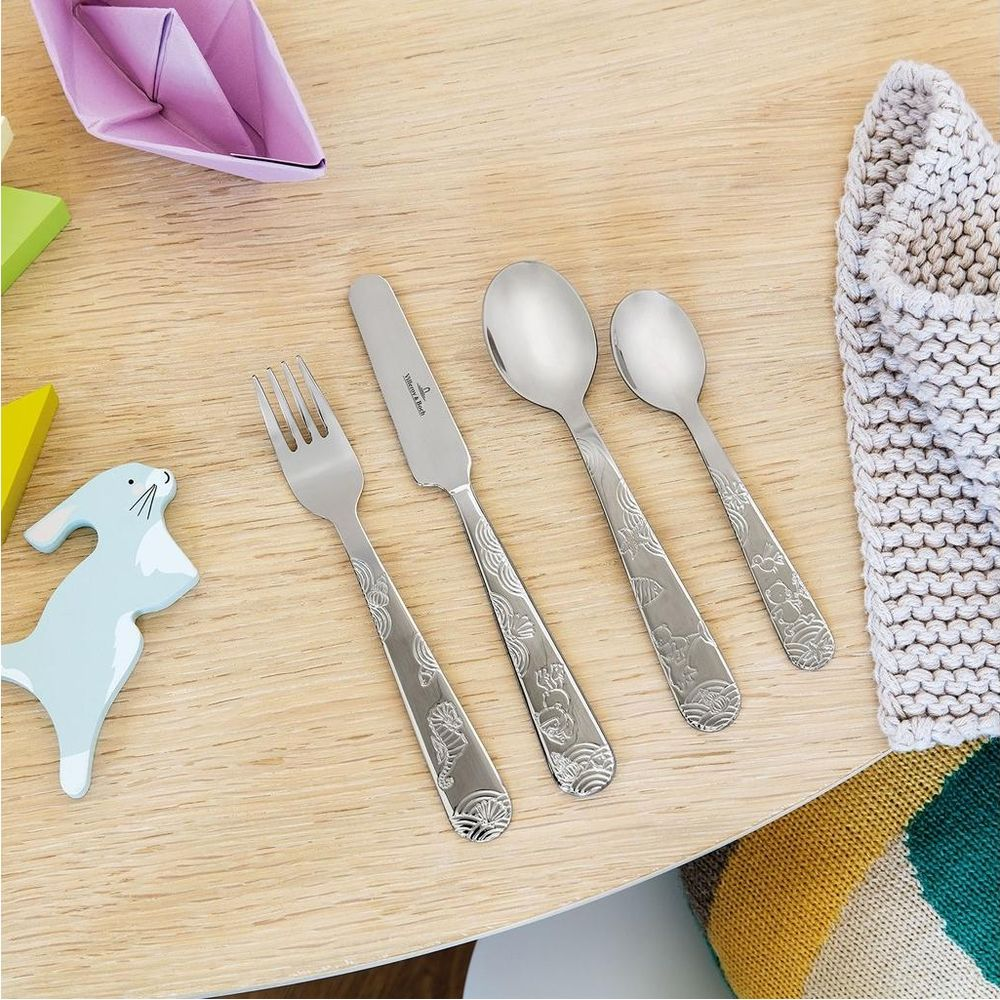 Silberbesteck mit Tiermotiven auf Holztisch neben Spielzeug und Strickware.