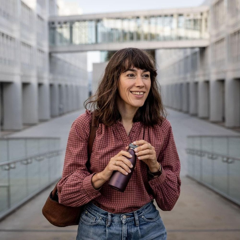 Eine Frau mit braunen Haaren hält eine lila Wasserflasche in einer modernen Architektur.