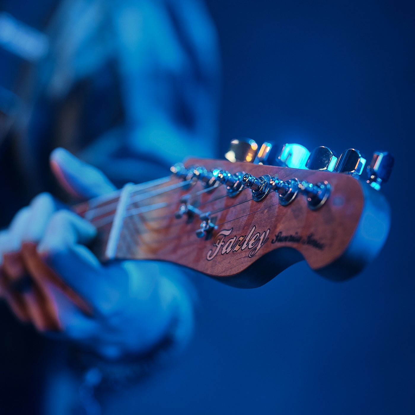 Close-up van een gitaarkop met snaren en stemmechanieken, verlicht met blauw licht.