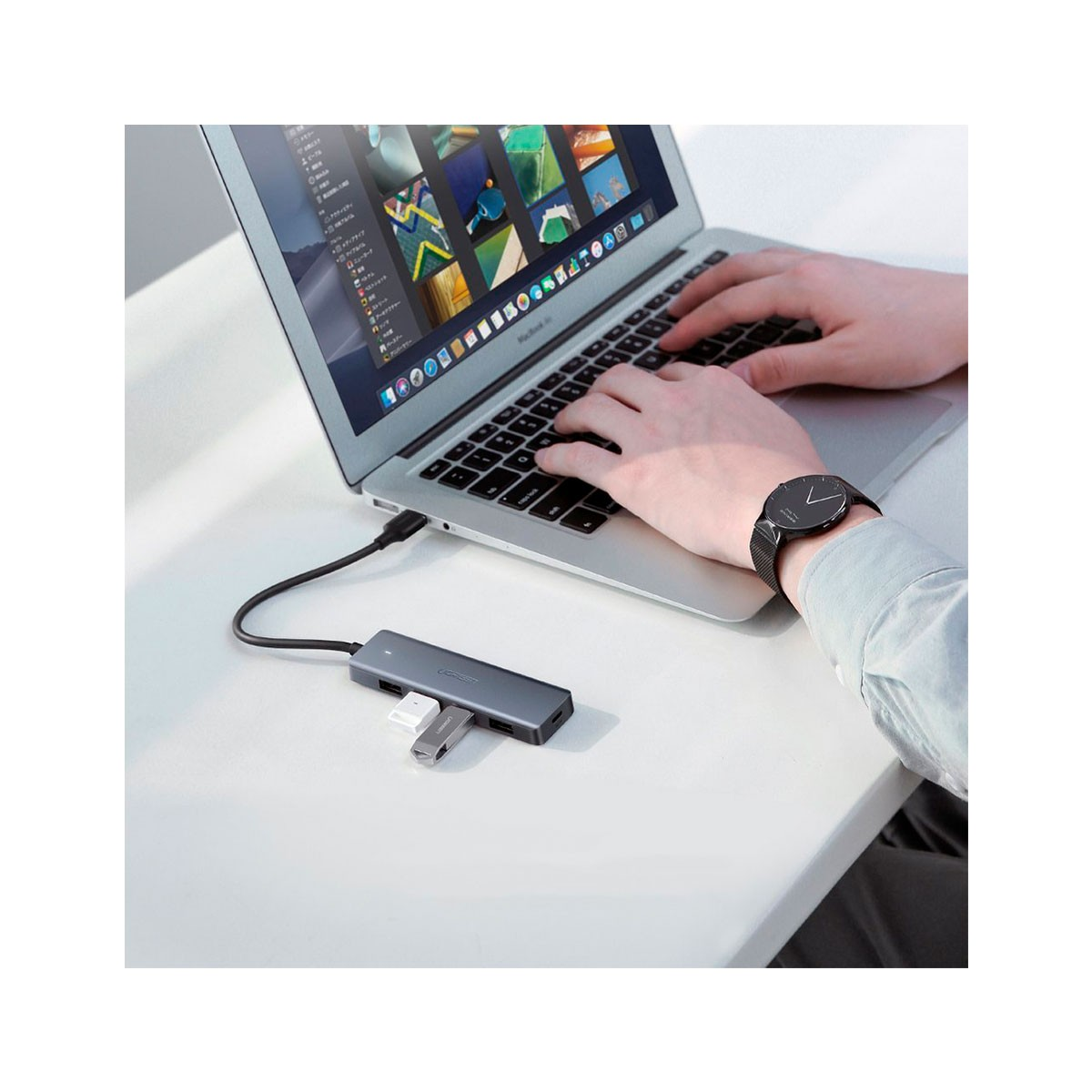 Szary hub USB-C z podłączonymi urządzeniami, obok laptopa, na którym ktoś pisze.