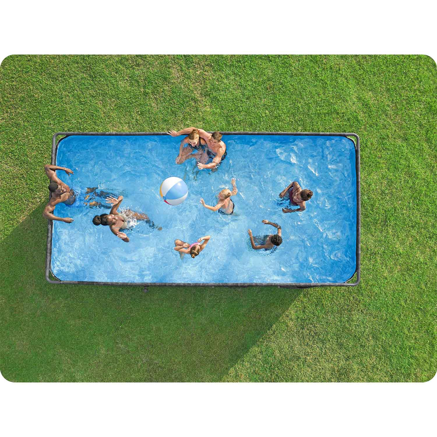 Siedem osób pluska w prostokątnym basenie otoczonym trawą. Piłka unosi się na wodzie.