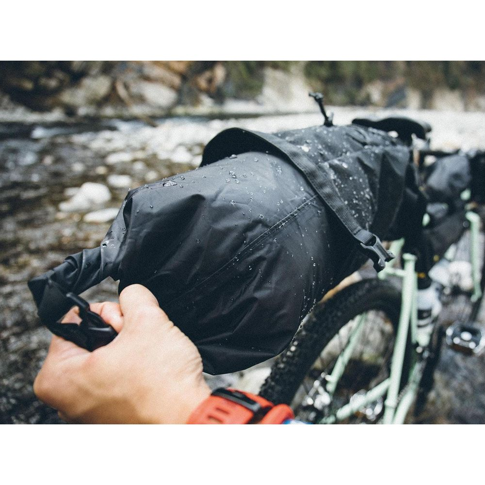 Une main tient un sac de vélo noir mouillé devant un vélo.