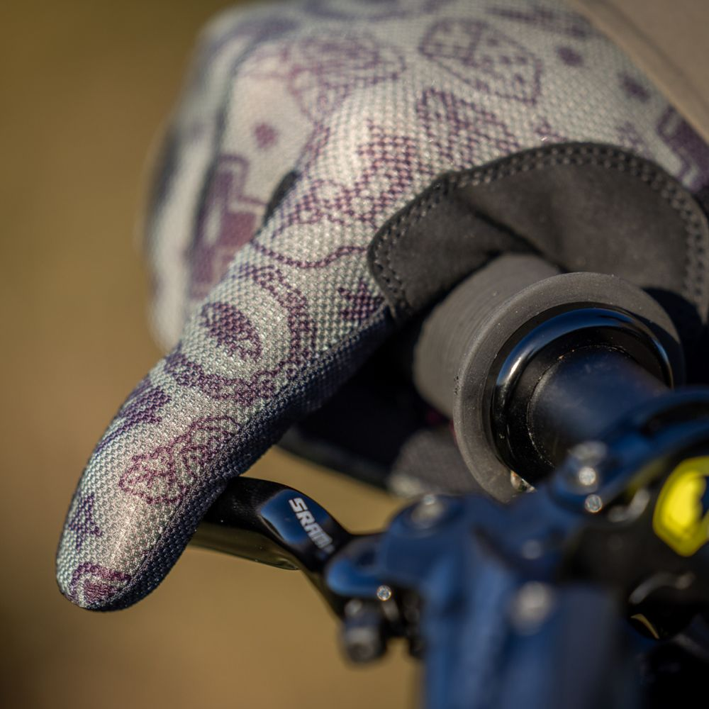Une main gantée à motif violet tient un guidon et un frein de vélo.