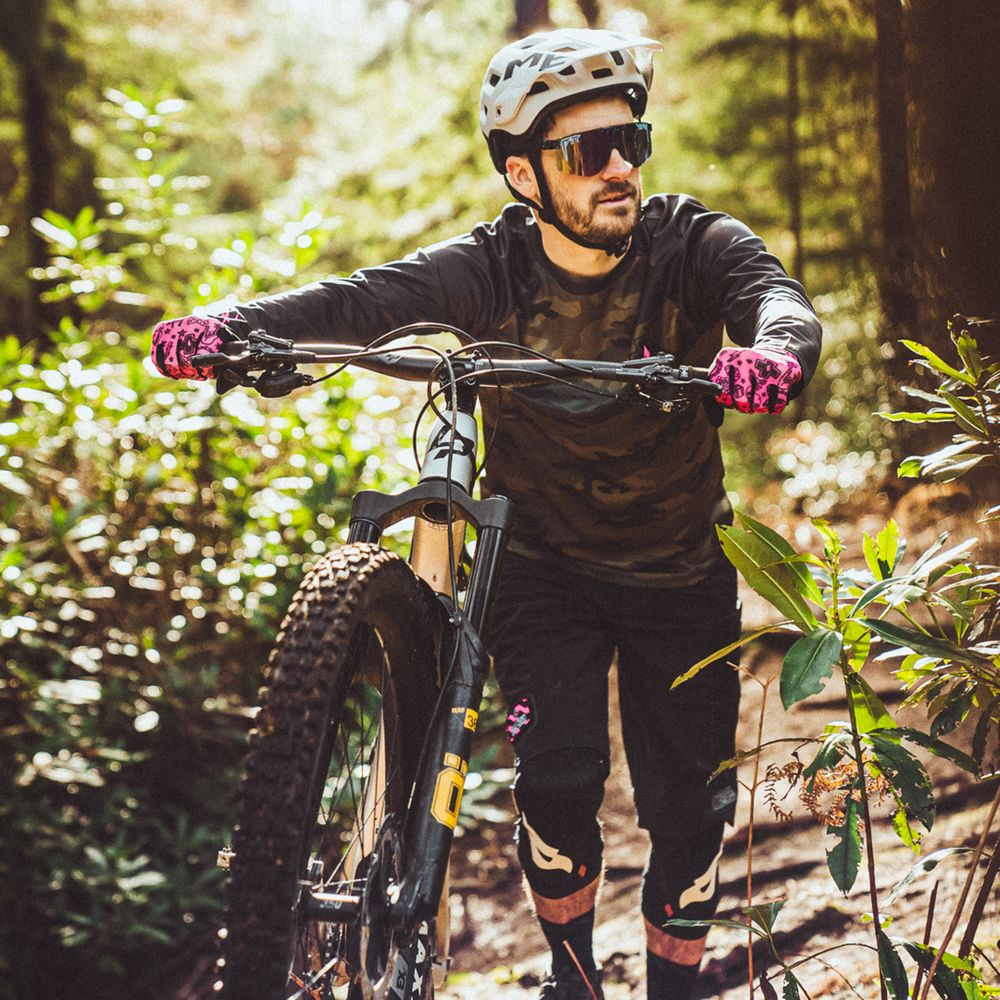 Ein Mann in voller Mountainbike-Ausrüstung schiebt sein Rad auf einem Waldweg.