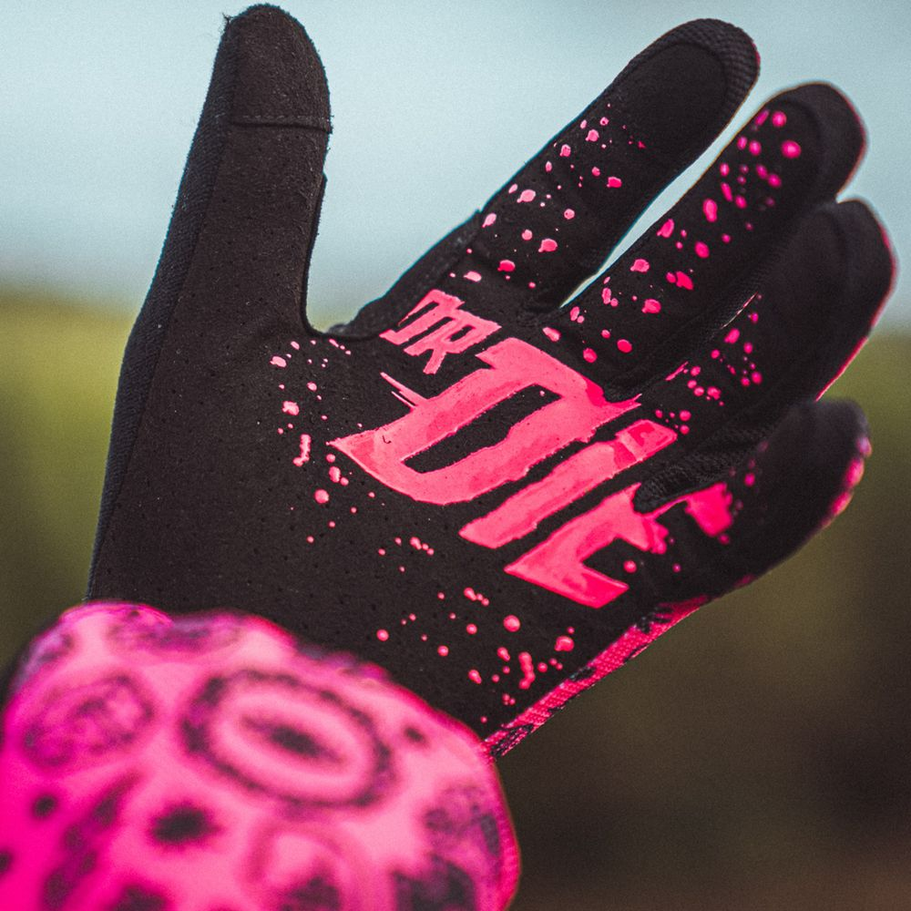 Schwarzer Handschuh mit pinken Spritzern und Logo, der auf einer Hand getragen wird.