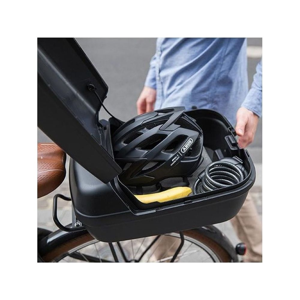 Ein schwarzer Helm und ein Schloss in einer Fahrradbox, die von einer Person geöffnet wird.