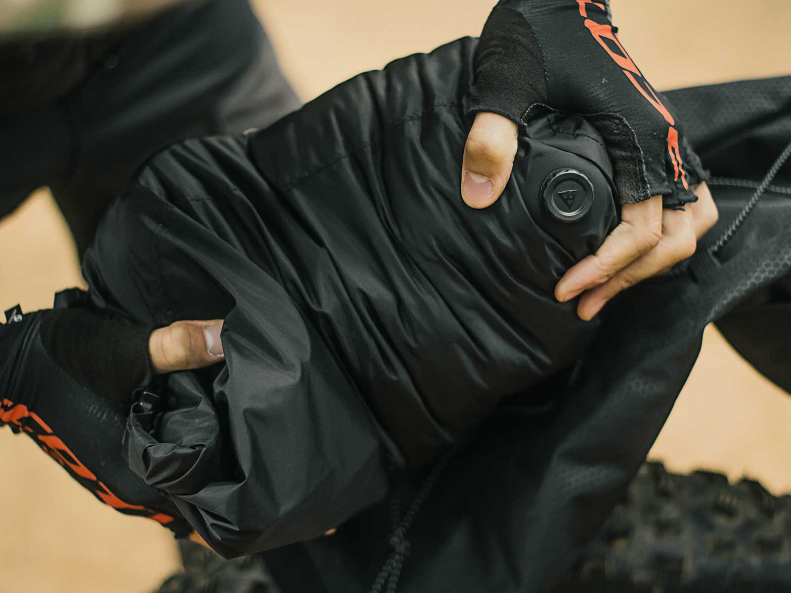 Mains gantées tenant une veste noire matelassée avec un bouton.