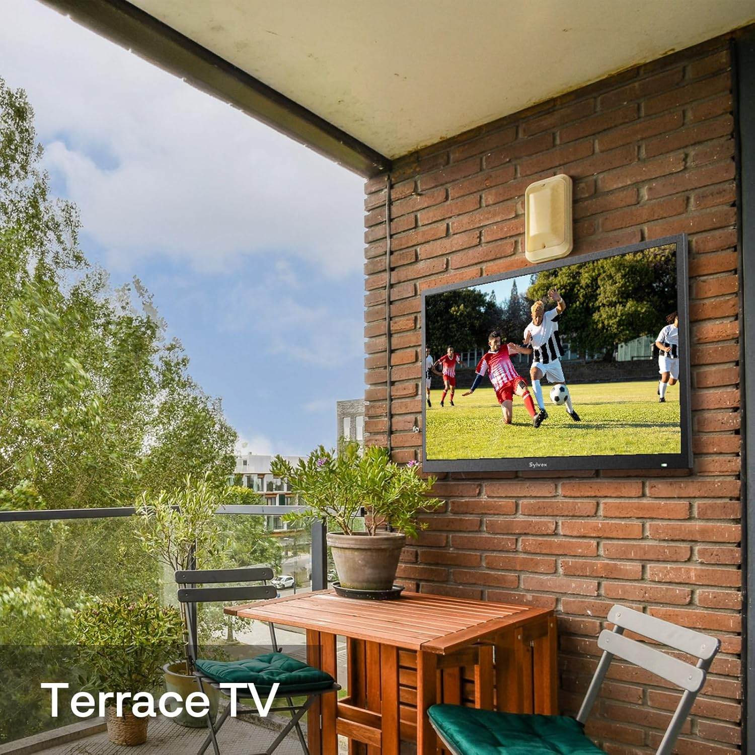 Un televisor en una pared de ladrillos muestra un partido de fútbol. Hay muebles en el balcón.