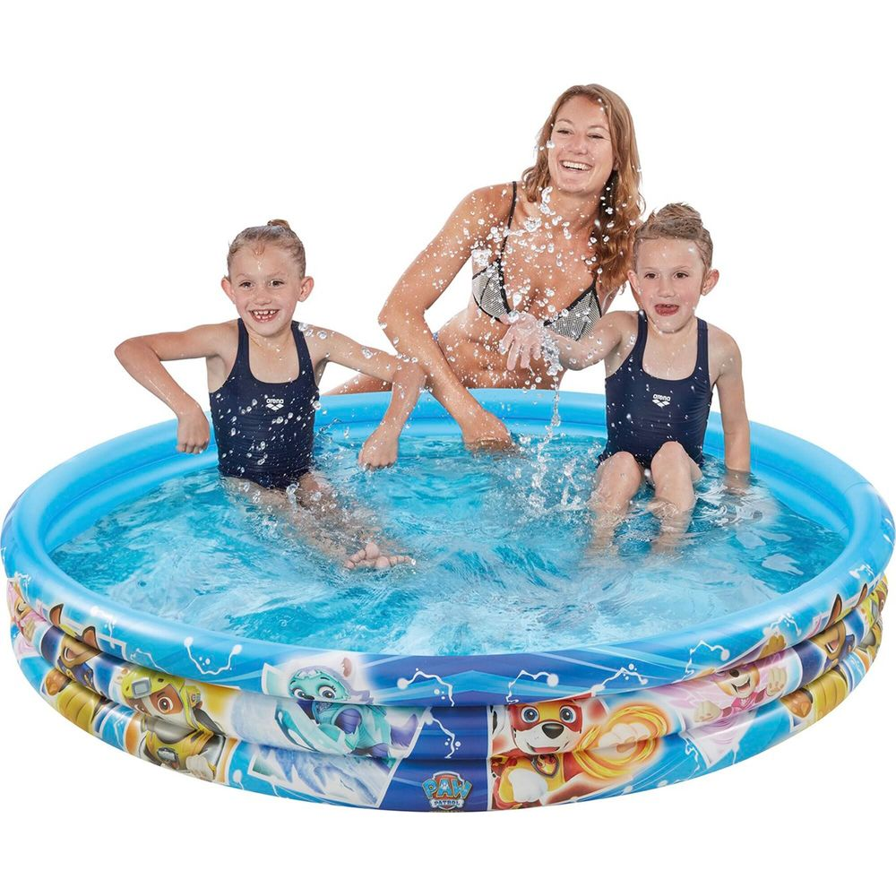 Trois personnes, deux enfants et un adulte, éclaboussant dans une piscine gonflable bleue décorée de personnages de dessins animés.