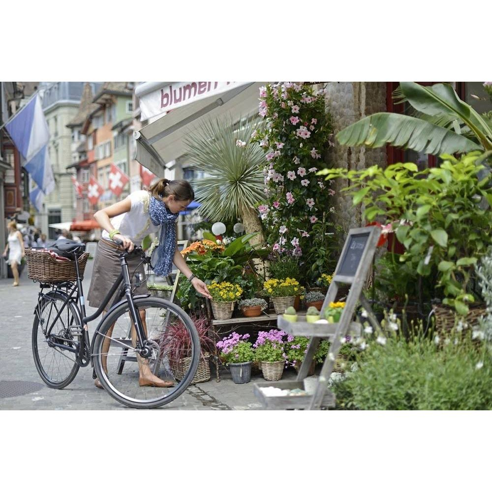 Una mujer con una bicicleta está frente a una floristería con muchas flores.