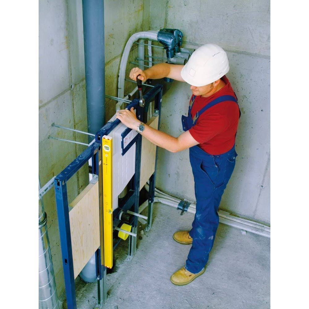 Ein Mann in blauer Latzhose und rotem Shirt montiert eine Toilette mit Werkzeug.