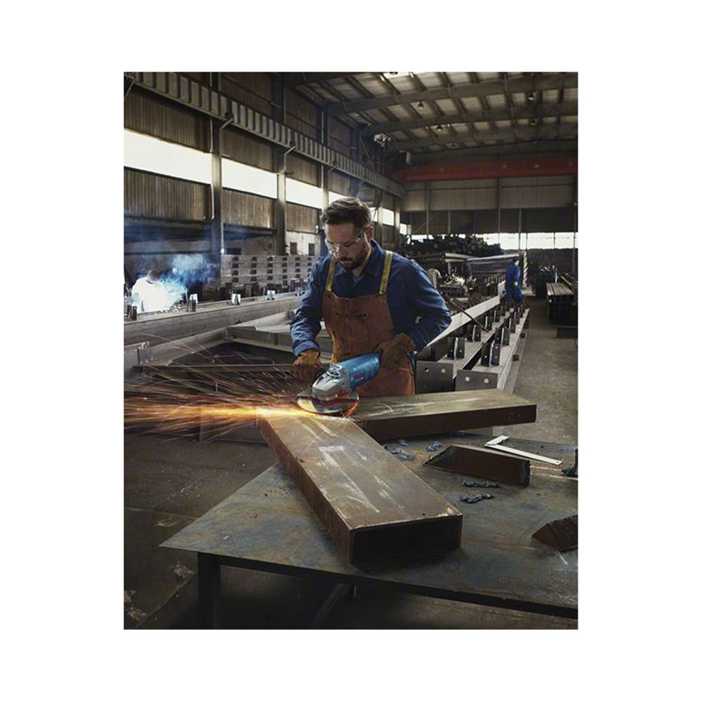 Homme meulant du métal en usine, étincelles jaillissent. Lunettes, tablier.