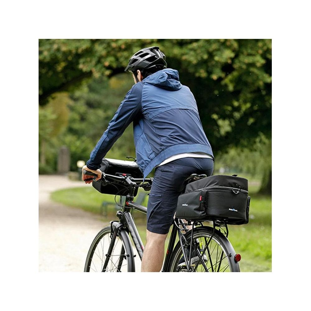 Mann mit Helm fährt Fahrrad mit Taschen vorne und hinten im Grünen.