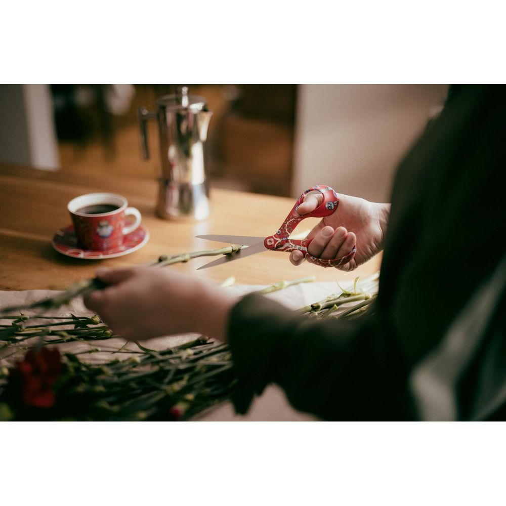 Eine Person schneidet Blumen mit roten Scheren auf einem Holztisch.