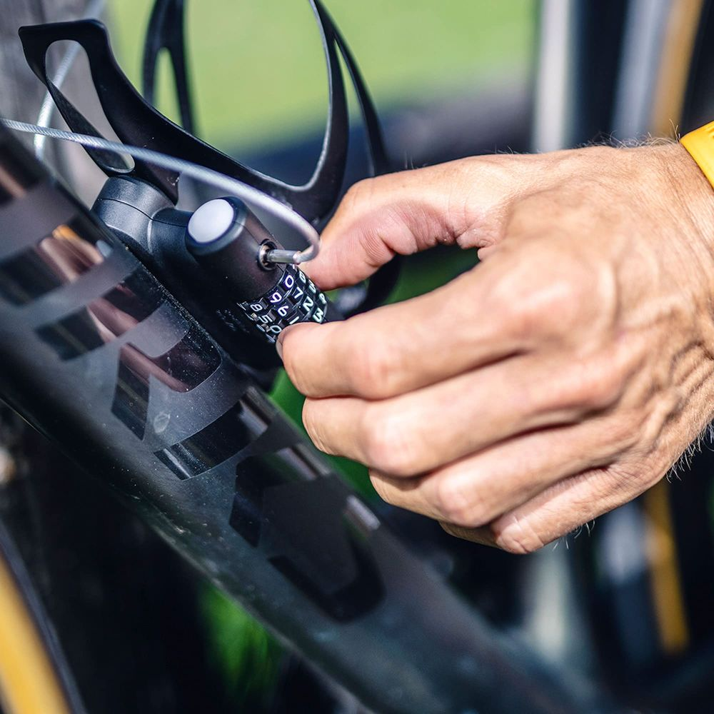 Eine Hand schließt ein schwarzes Fahrradschloss mit Zahlenkombination an einem Fahrradrahmen.