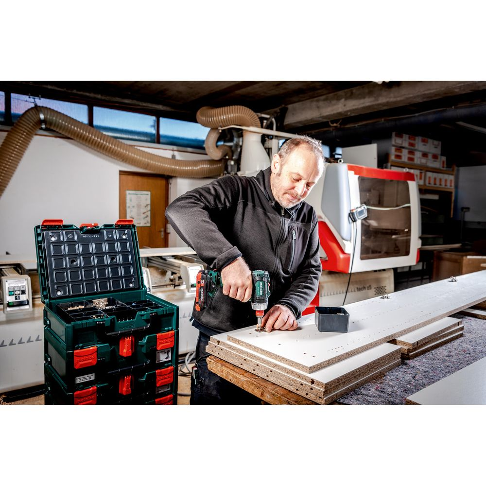 Ein Mann schraubt mit einem Akkuschrauber Holzplatten zusammen. Werkzeugkasten daneben.