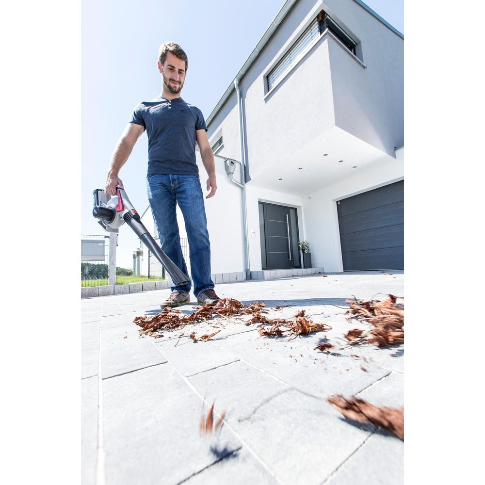 Uomo soffia foglie con soffiatore su vialetto pavimentato davanti a casa moderna.