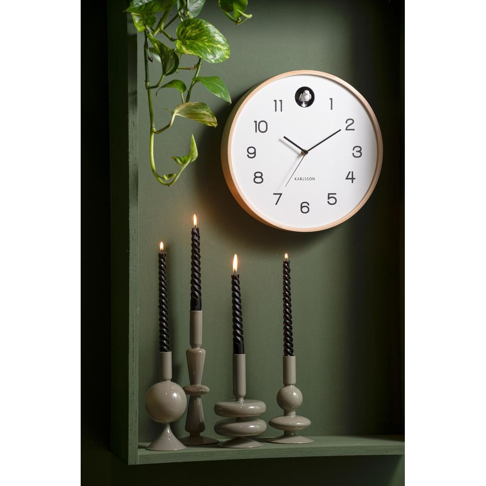 Ein runder Karlsson-Wanduhr mit einem Holzkranz hängt über vier schwarzen Kerzen auf Kerzenständern.