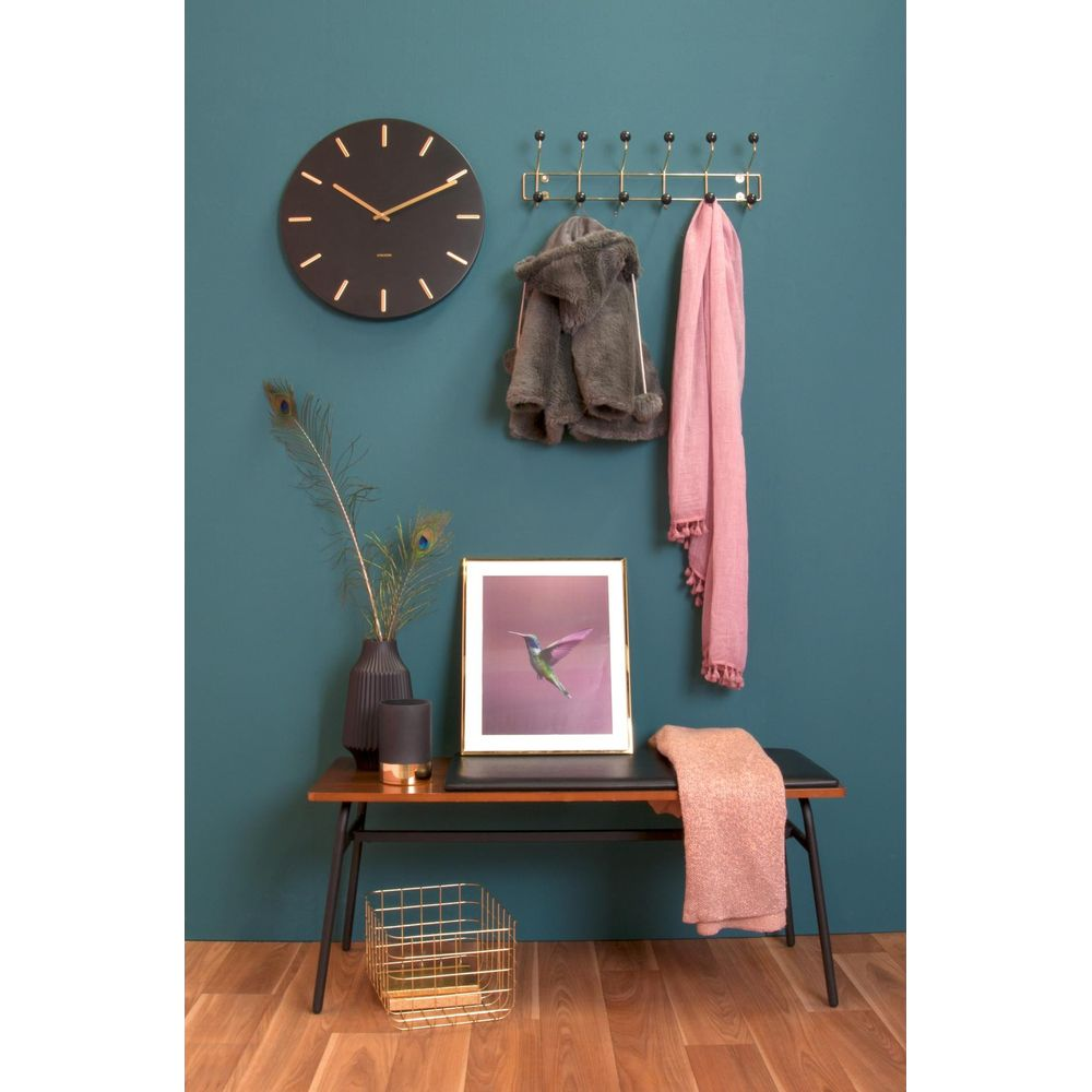 Eine dunkle Wand zeigt eine Uhr, eine Garderobe mit Gegenständen und gerahmte Kunst eines Kolibris.