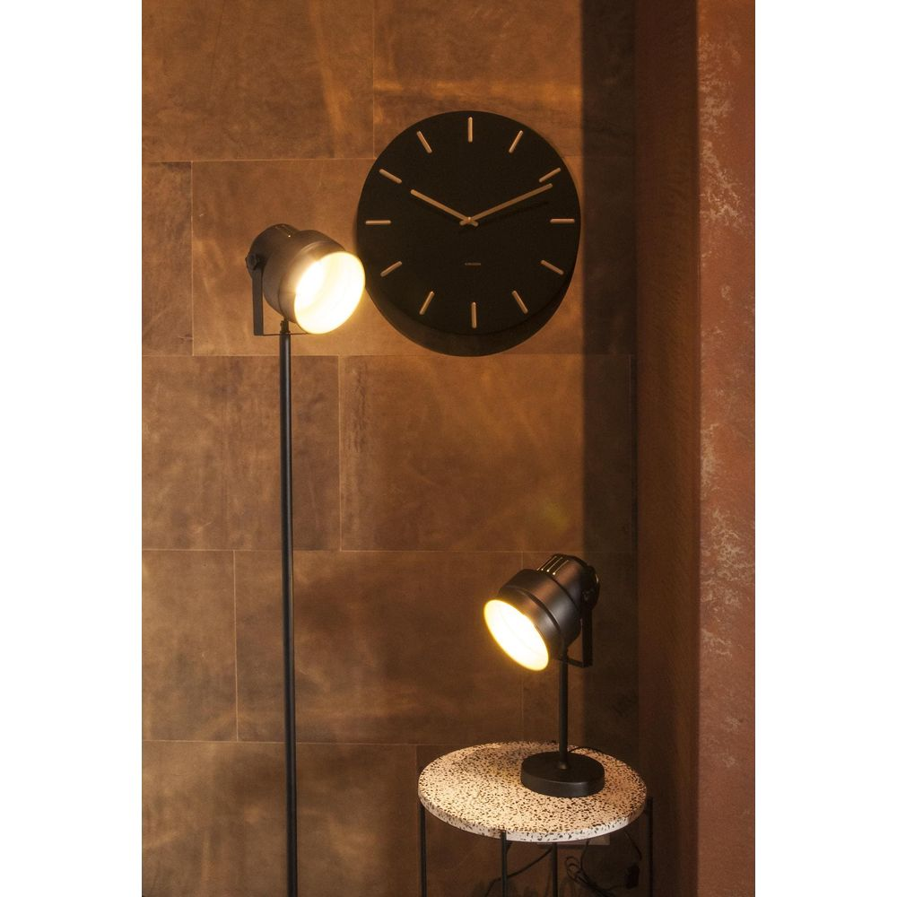 Ein schwarzer runder Wanduhr über einem Stehlampen und einem Tischlampen auf einem runden Tisch.