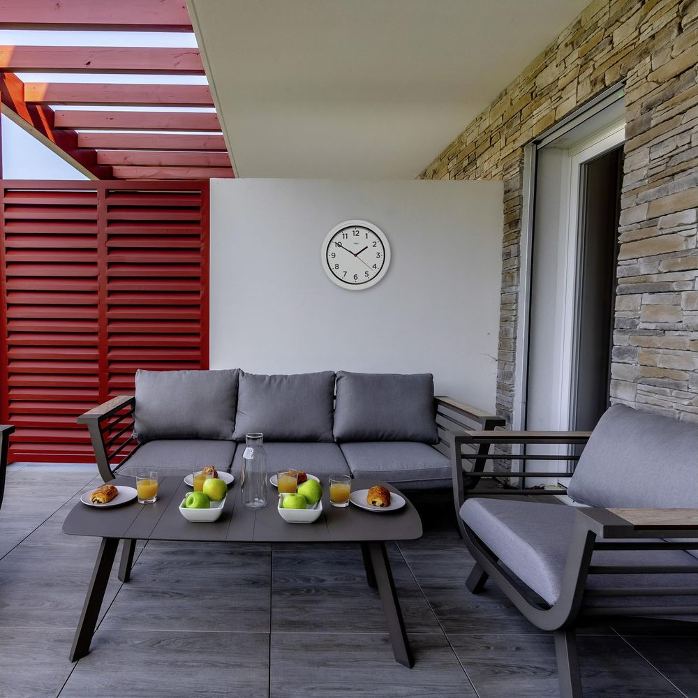 Ein moderner Balkon mit grauen Sofas, einem Tisch mit Frühstück und einer Uhr.