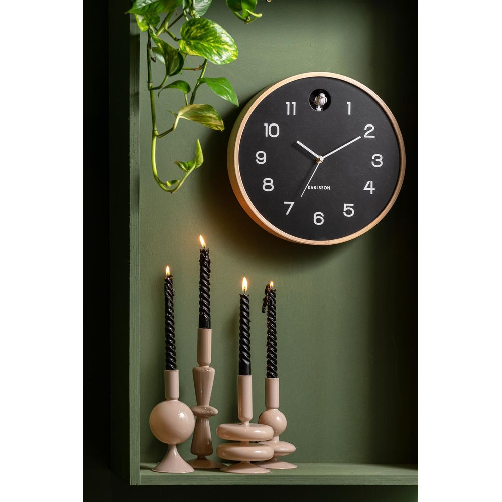 Schwarze Kerzen auf Beigefarbenen Kerzenhaltern vor einer grünen Wand und einer Uhr.