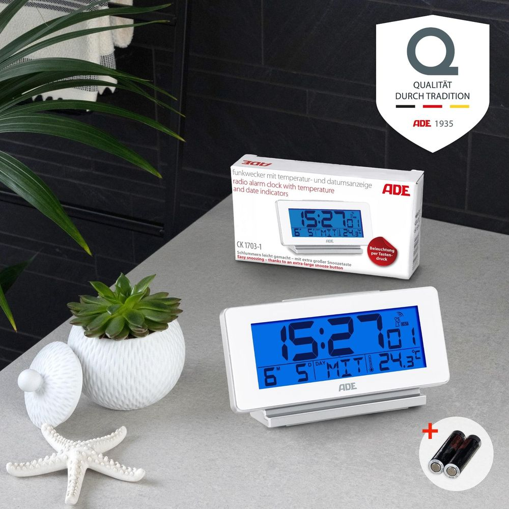 Un radio-réveil blanc avec écran bleu affiche 15:27 et 24,3°C.