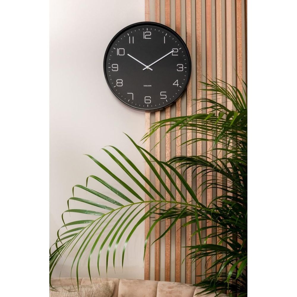 Eine schwarze Wanduhr mit weißen Ziffern hängt an einer Wand mit Holzlatten.