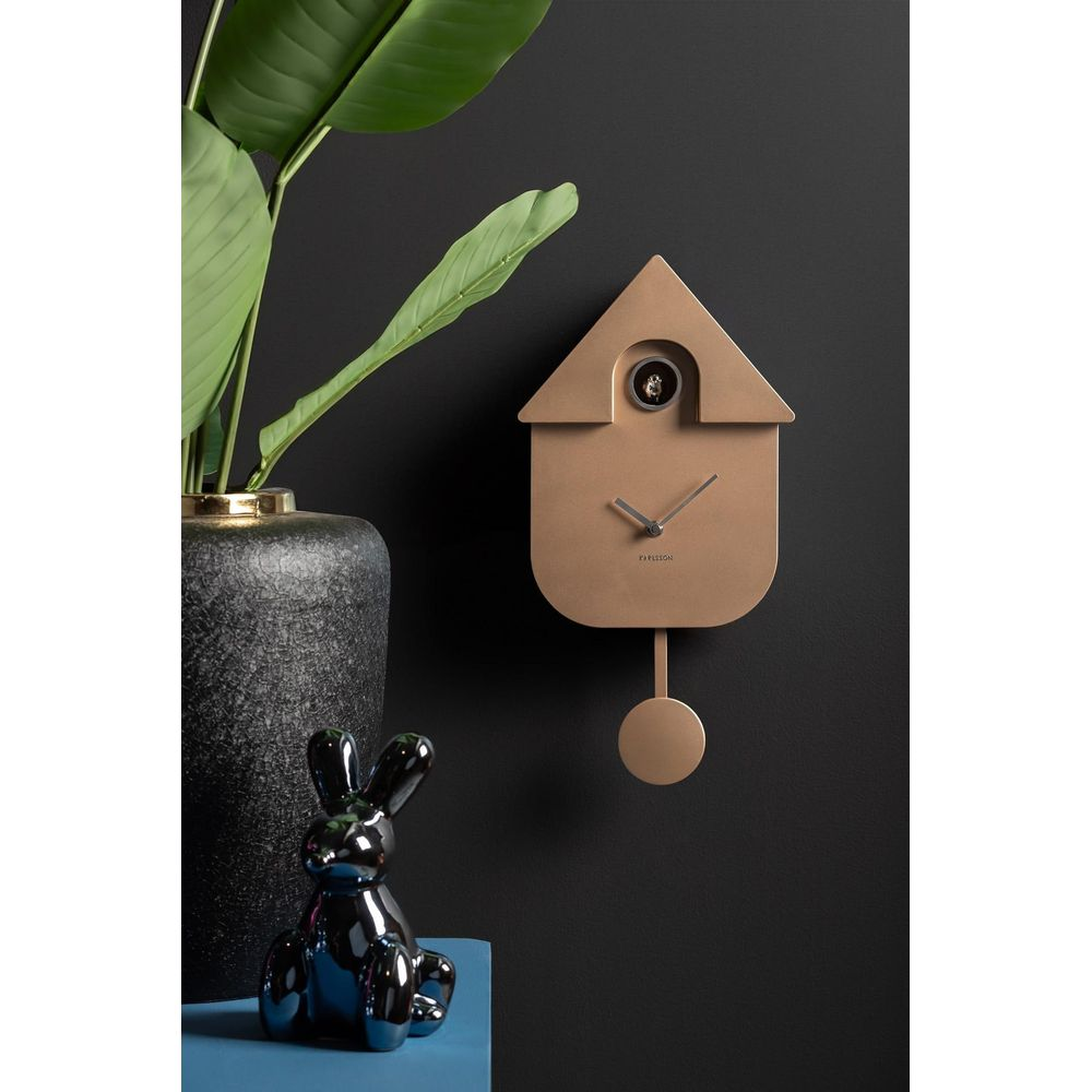 Une horloge coucou dorée avec pendule sur mur noir, près d'une grande feuille et d'un lapin.