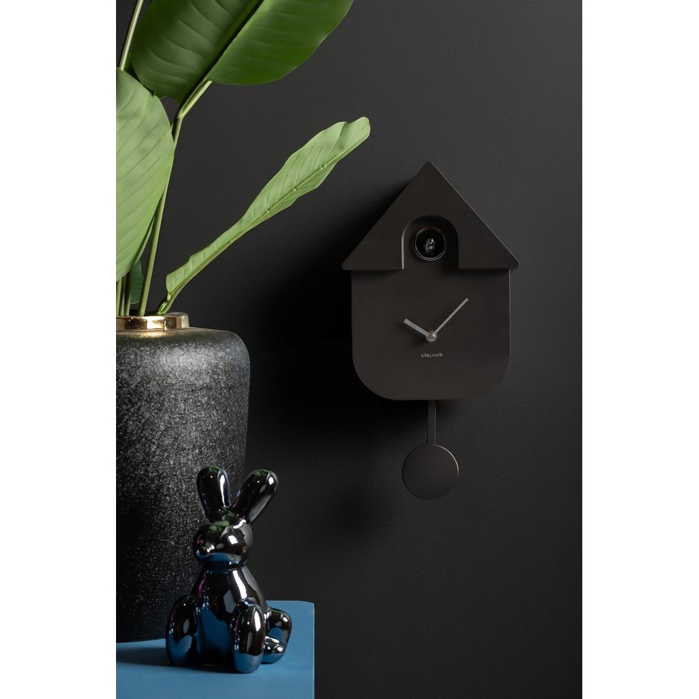 Un orologio da parete nero stile orologio a cucù con statuetta di coniglio e pianta.