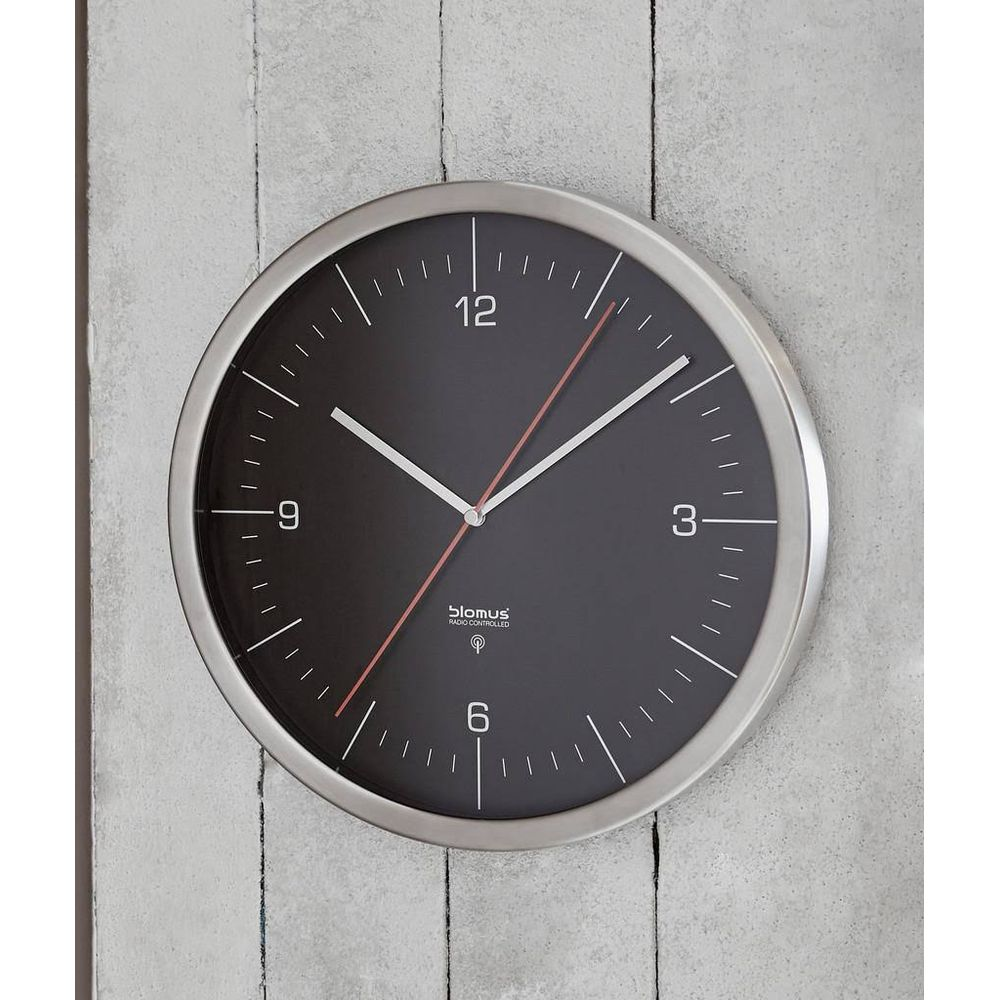Eine schwarze Wanduhr mit silbernem Rahmen hängt an einer Wand.