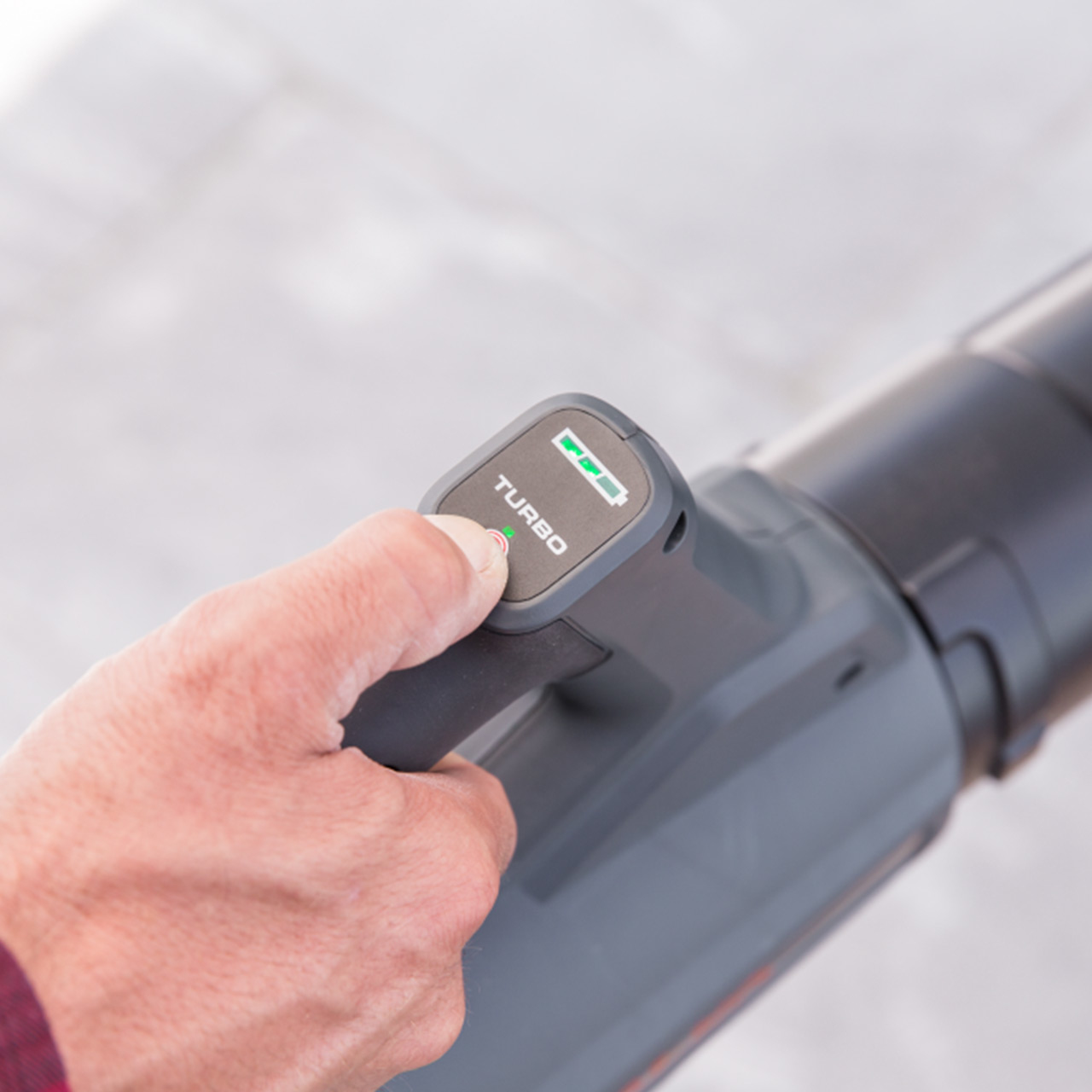 Ein Finger drückt auf den TURBO-Knopf eines Laubbläsers mit voller Batterieanzeige.