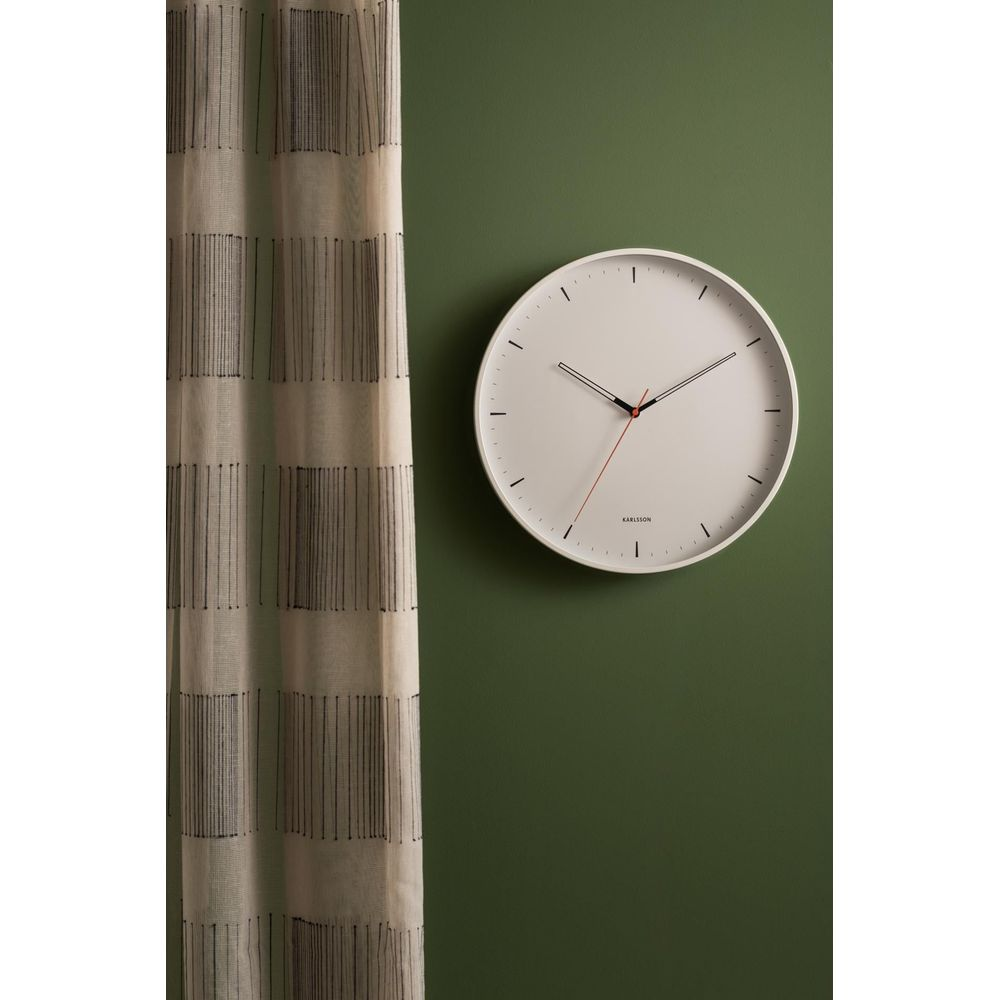 Un orologio da parete bianco con lancette nere è appeso a una parete verde scuro accanto a una tenda.