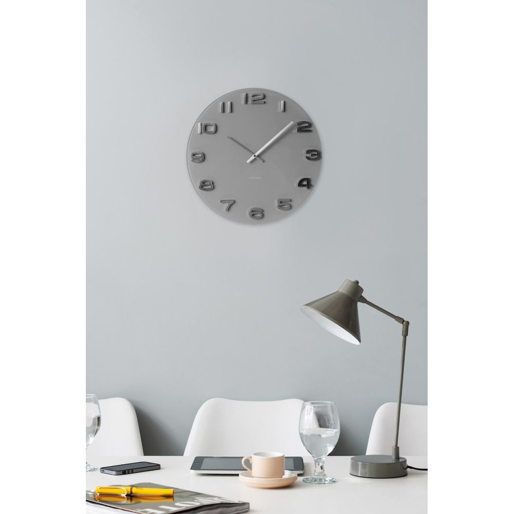 Un orologio da parete grigio con numeri appeso sopra una scrivania con lampada.