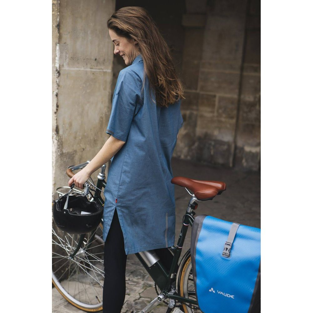 Eine Frau mit langen braunen Haaren steht neben einem Fahrrad mit einer blauen Tasche.