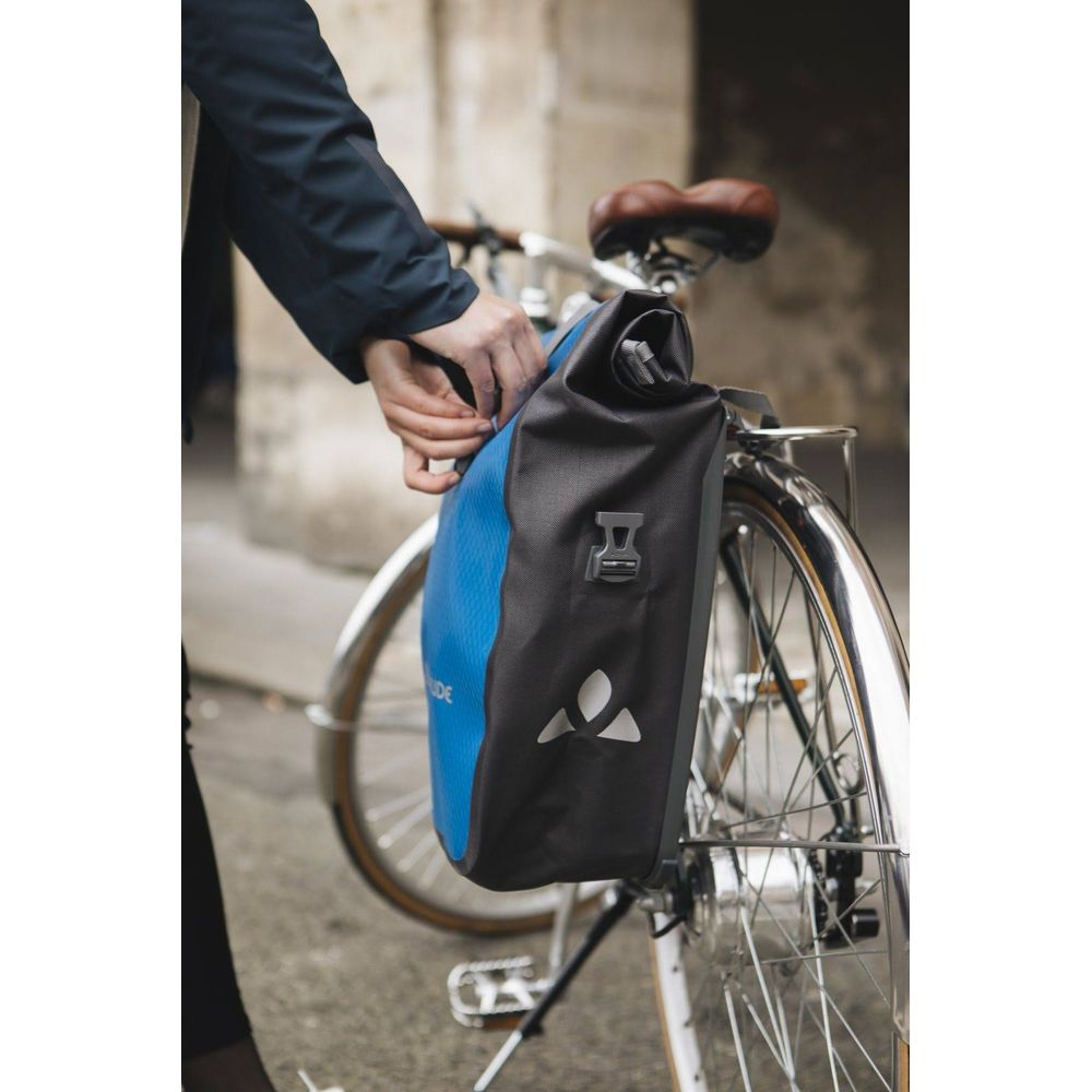 Person befestigt blaue Fahrradtasche mit schwarzem Verschluss am Gepäckträger.