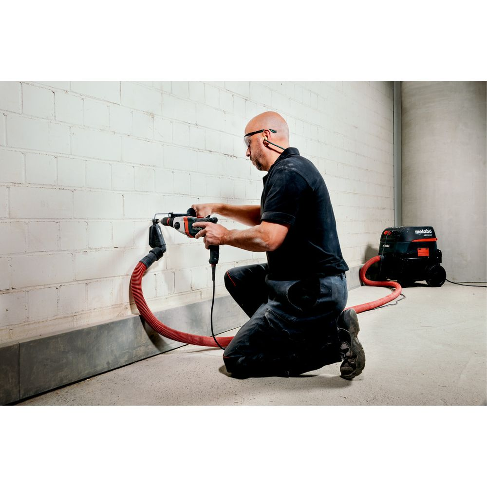 Homme perce mur en brique blanche, relié à un aspirateur.