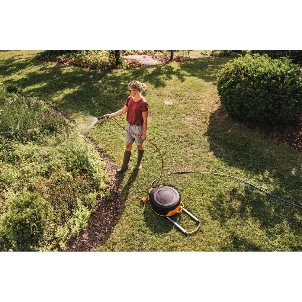 Eine Frau wässert einen Garten mit einem Schlauch von einem aufgerollten Schlauchwagen.
