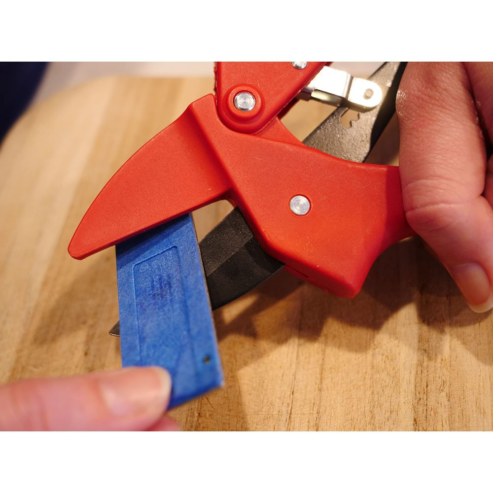 Pinces rouges coupant du ruban bleu sur surface en bois.