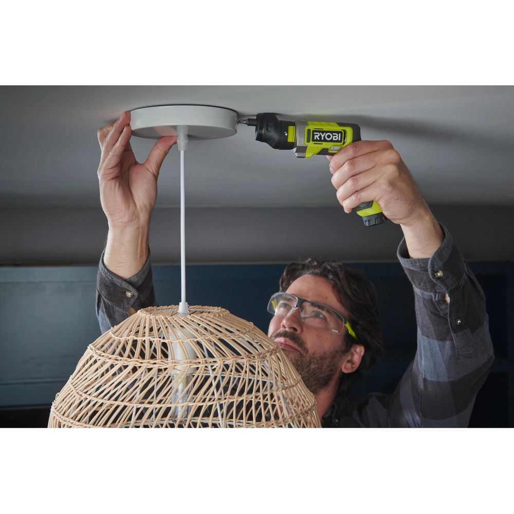 Mann montiert Lampe mit Schrauber an Decke. Rattan-Schirm.