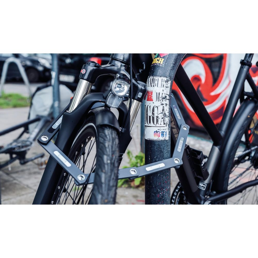 Ein schwarzes Fahrrad ist mit einem Faltschloss an einem Pfosten gesichert.