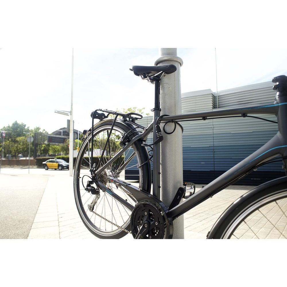 Ein dunkelgraues Fahrrad ist an einem Laternenpfahl auf einem Bürgersteig angeschlossen. Ein gelber Taxi ist im Hintergrund.