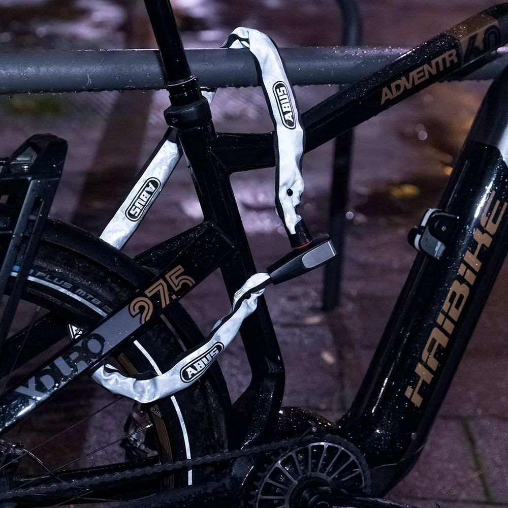Ein schwarzes E-Bike ist mit einer weißen Kette an einem Gitter angeschlossen.