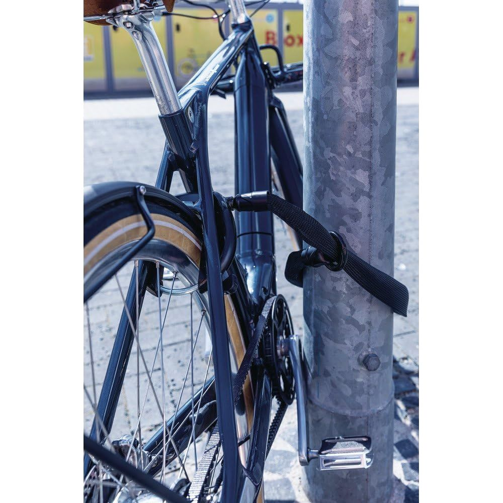 Ein dunkles Fahrrad ist mit einem schwarzen Schloss an einer Laterne angeschlossen.