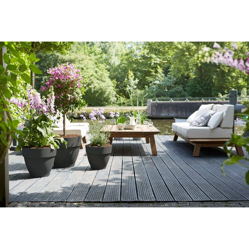 Eine Terrasse mit Möbeln und Pflanzen am Wasser.