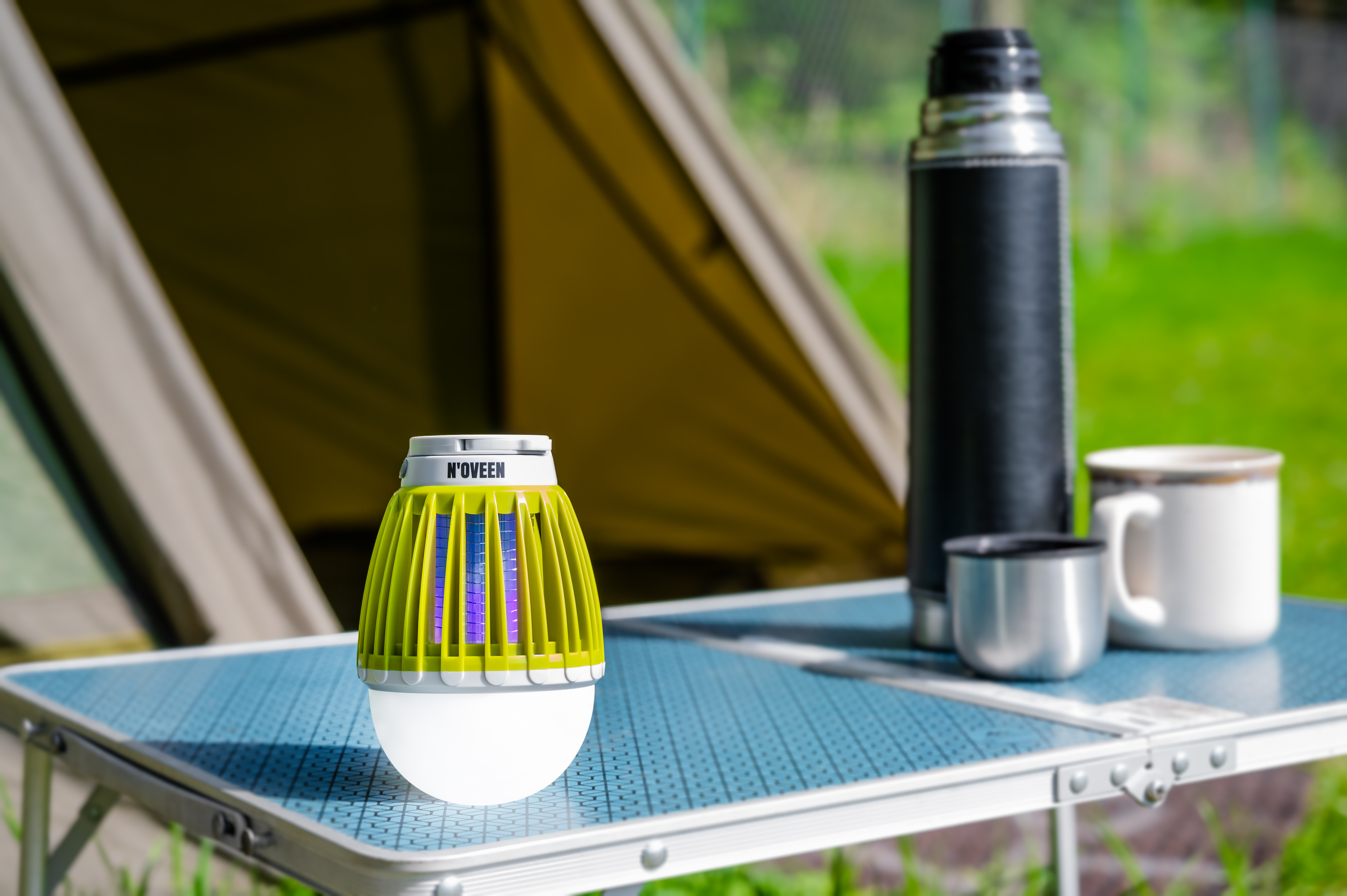 Zielona lampa na owady, termos i kubek na stole kempingowym.