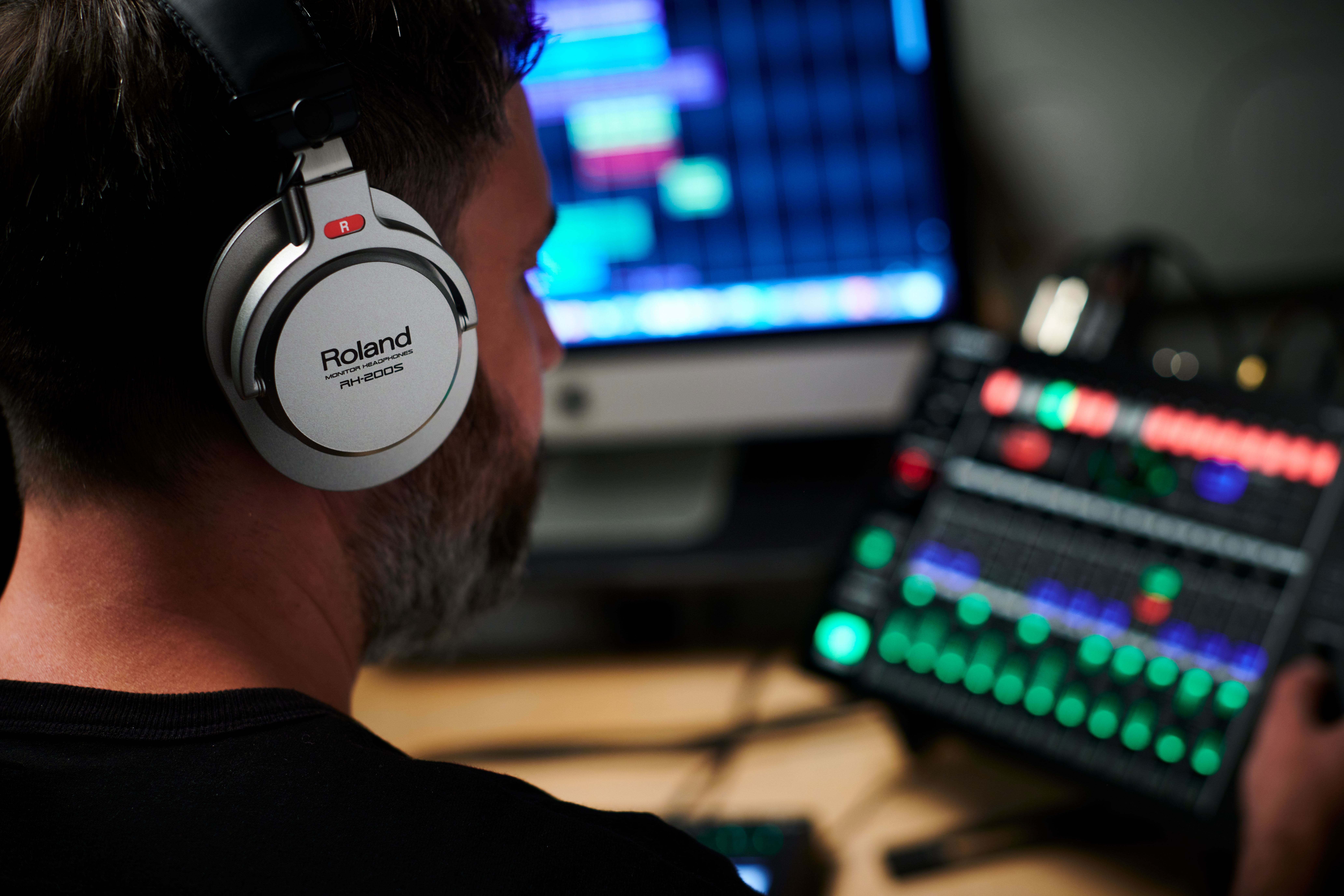 Homme portant des écouteurs devant une table de mixage et un écran d'ordinateur.