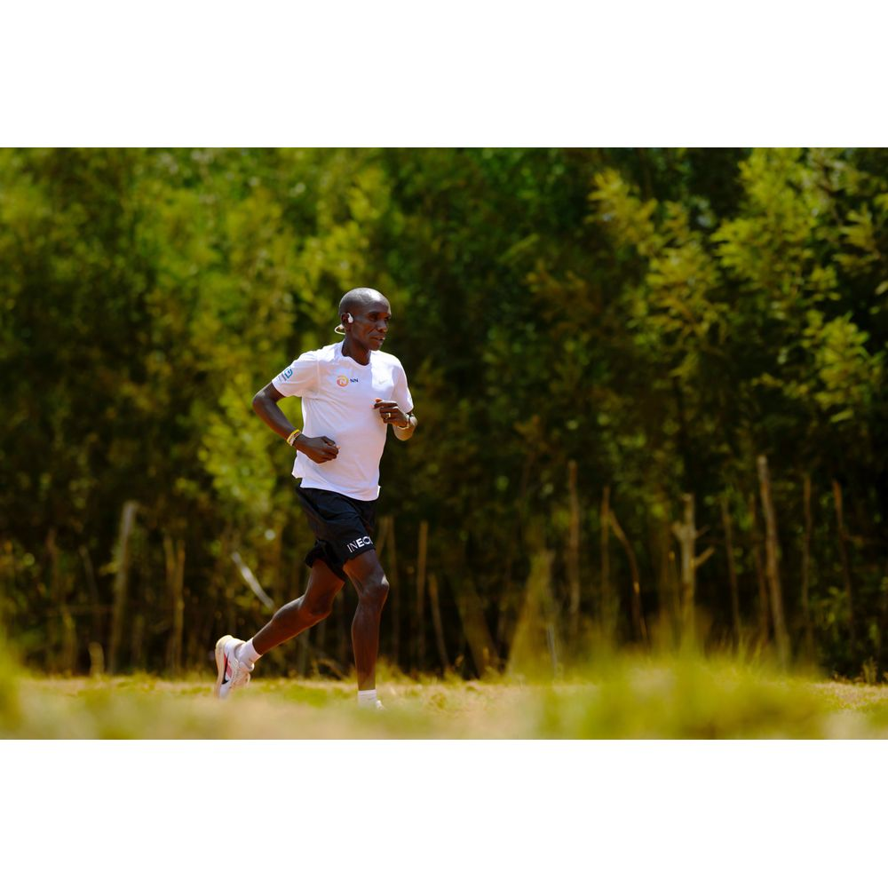 Mężczyzna w bieli i czerni biegnie po polu z drzewami w tle.