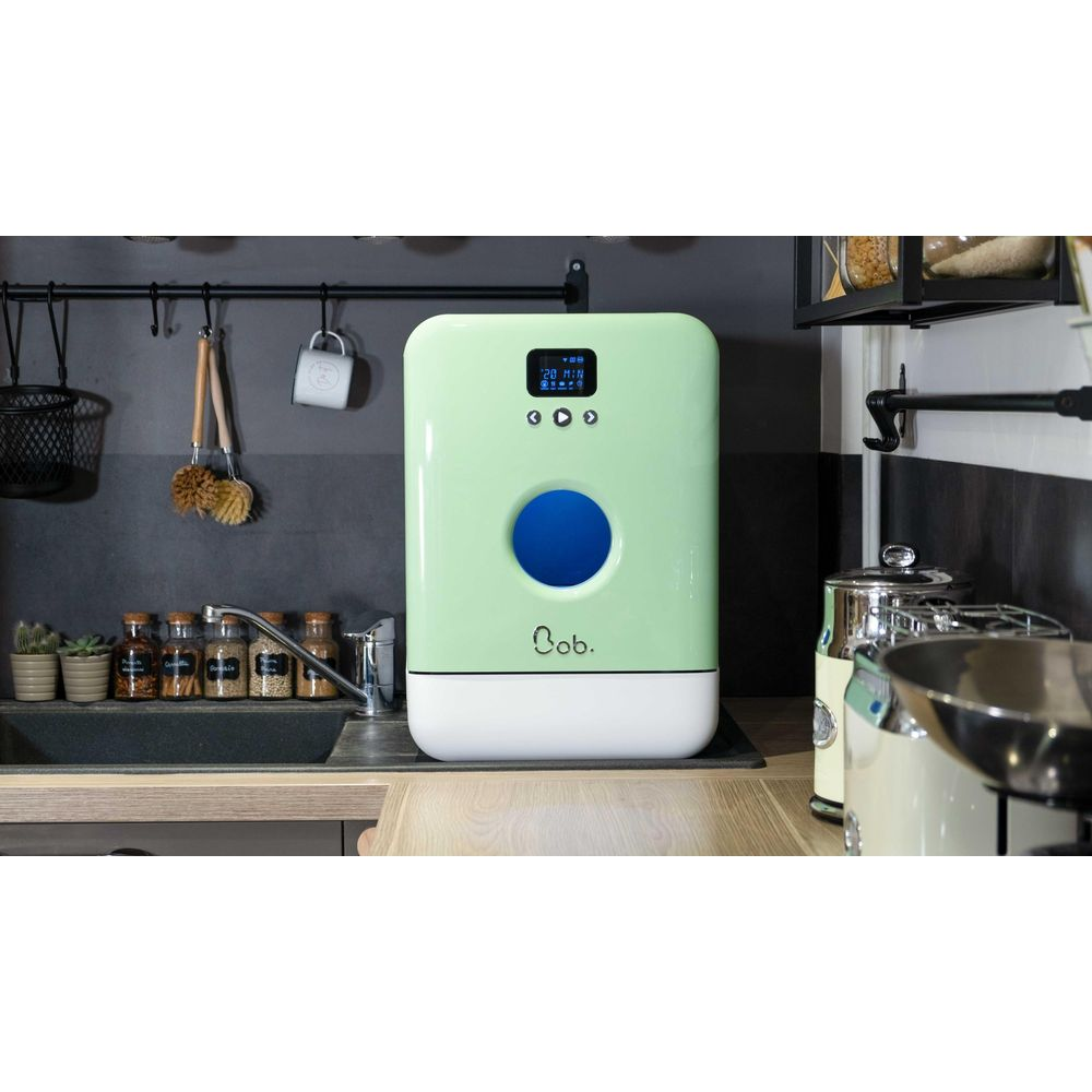 Una lavastoviglie verde chiaro con cerchio blu si trova su un bancone vicino a un lavello.