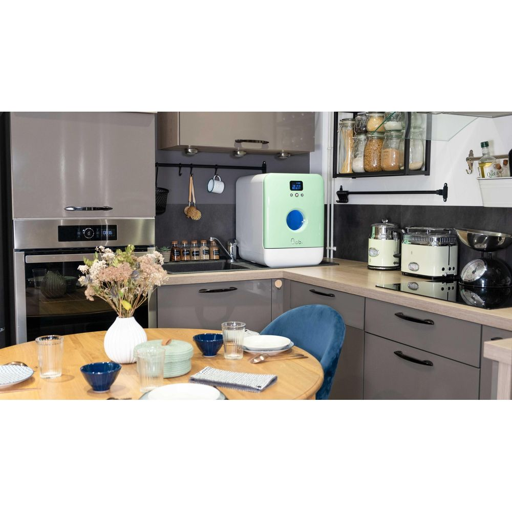 Una mini lavastoviglie verde si trova sul bancone della cucina accanto a un forno.